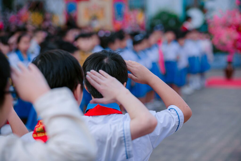 Group of children in uniform saluting together during a school assembly outdoors.